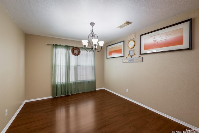 spare room with visible vents, dark wood finished floors, a notable chandelier, and baseboards