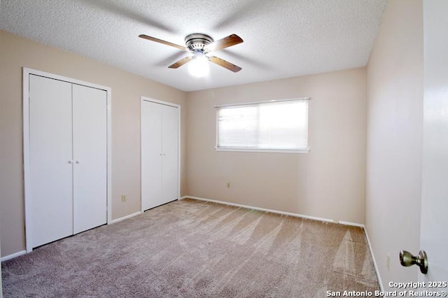 unfurnished bedroom featuring multiple closets, carpet, a textured ceiling, and a ceiling fan