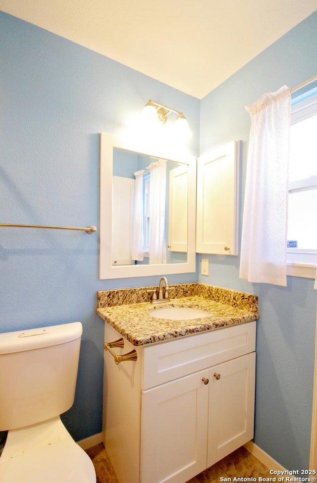 half bathroom with baseboards, vanity, and toilet