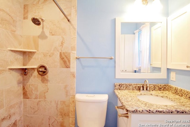 bathroom featuring toilet, tiled shower, and vanity