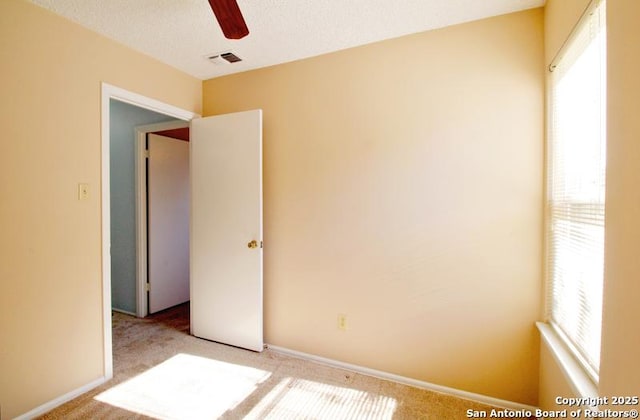 spare room featuring a textured ceiling, a wealth of natural light, carpet, and visible vents