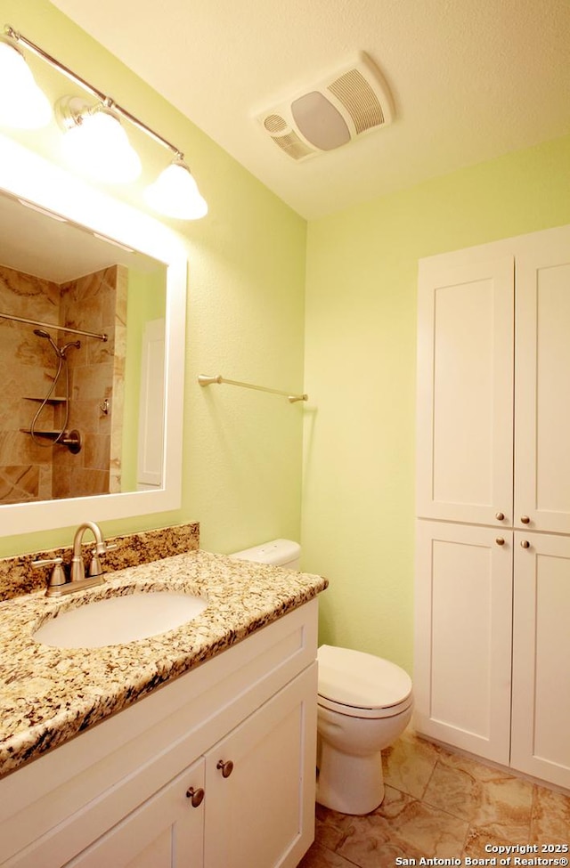 bathroom featuring toilet, tiled shower, vanity, and visible vents