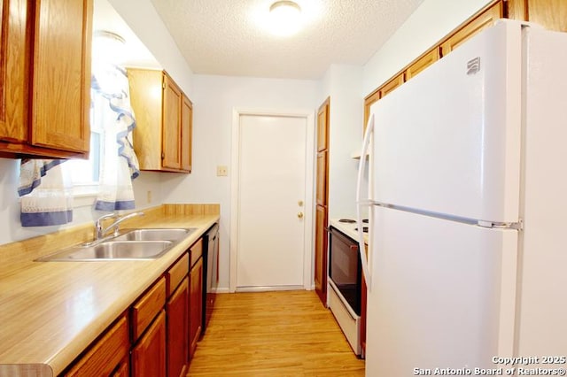 kitchen featuring dishwashing machine, stove, freestanding refrigerator, light countertops, and a sink