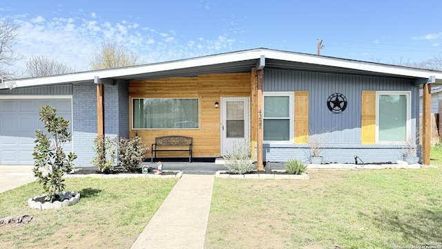 view of front facade with covered porch, brick siding, a front lawn, and an attached garage