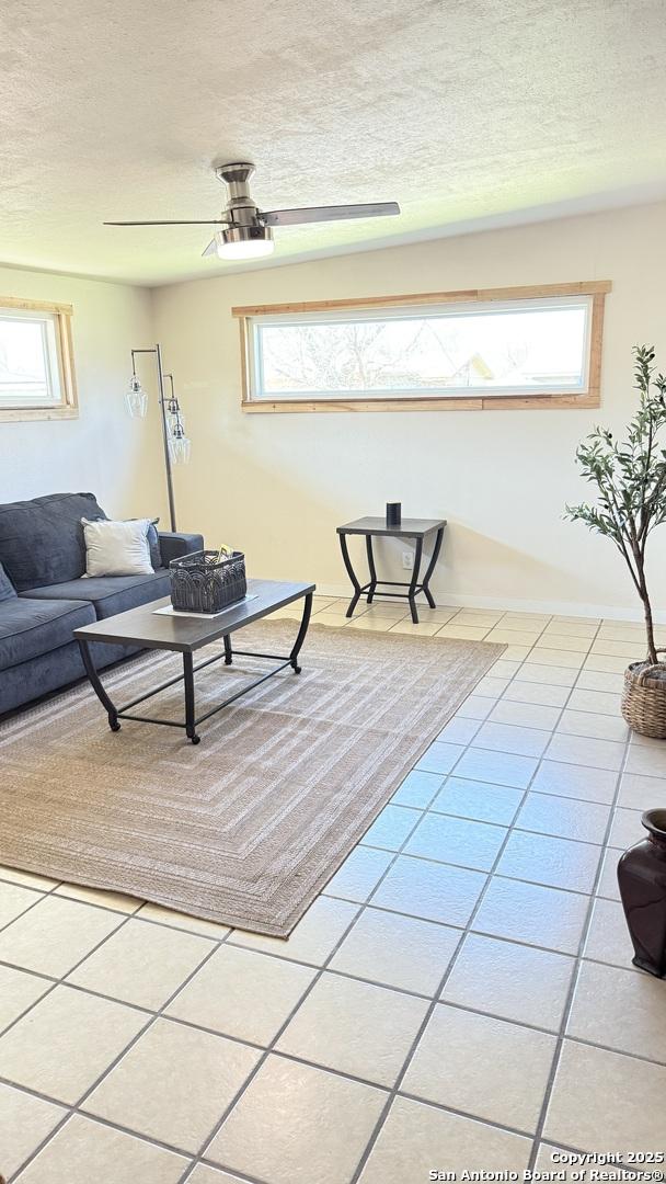 living room featuring ceiling fan, a textured ceiling, and light tile patterned floors