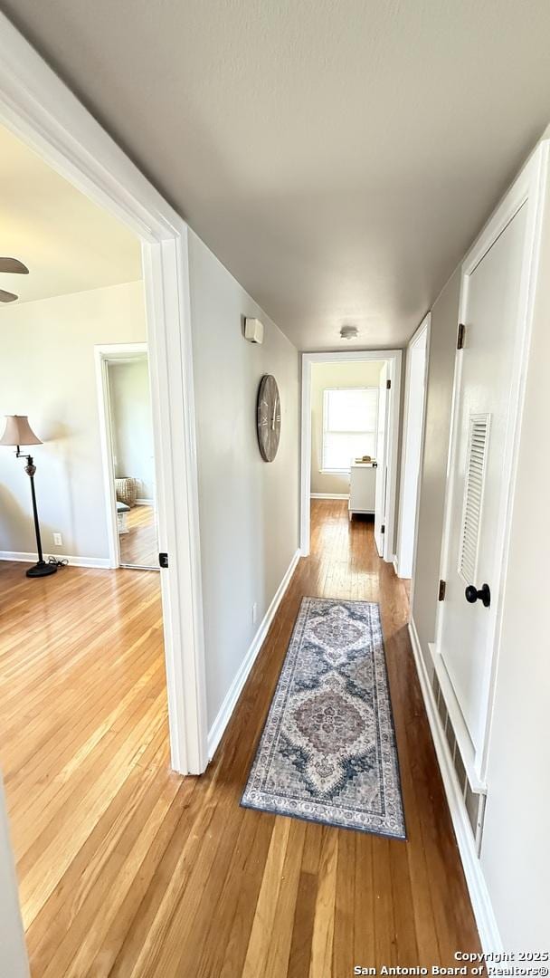 hallway featuring wood-type flooring, visible vents, and baseboards