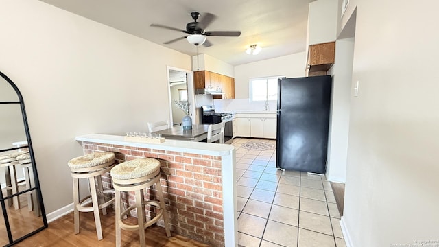 kitchen with light tile patterned floors, light countertops, freestanding refrigerator, a peninsula, and stainless steel gas range oven