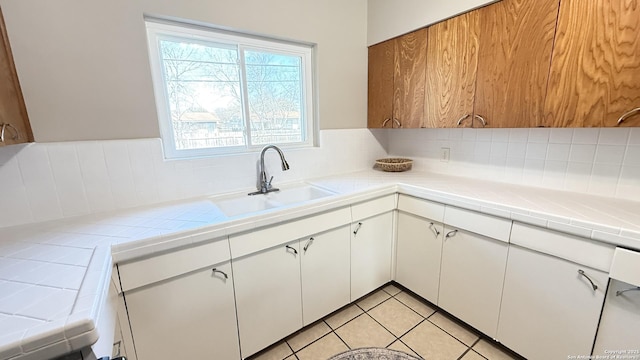 kitchen featuring light tile patterned floors, decorative backsplash, tile countertops, white cabinetry, and a sink