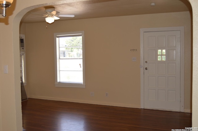 foyer with arched walkways, dark wood-style floors, a ceiling fan, and baseboards