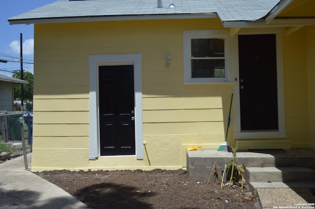 property entrance featuring a shingled roof and fence