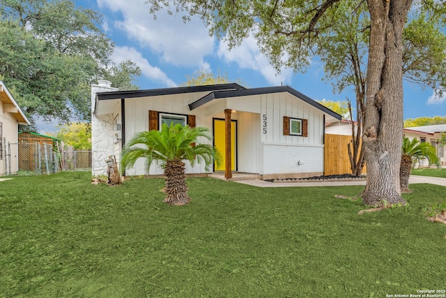 view of front of home with board and batten siding, fence, and a front lawn