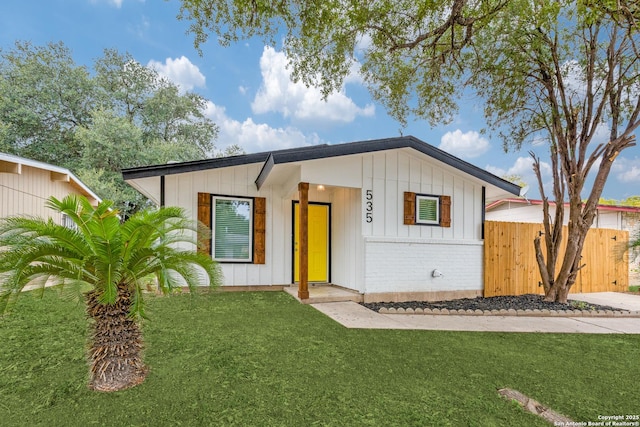 view of front of home with a front lawn, board and batten siding, fence, and brick siding