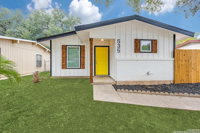 view of front of house with brick siding, board and batten siding, a front yard, and fence