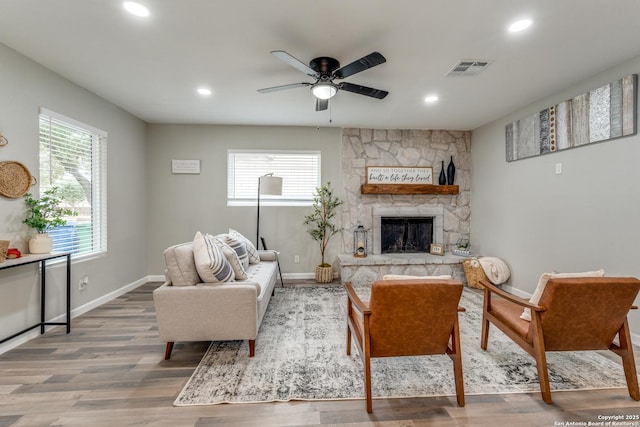 living room with a stone fireplace, wood finished floors, visible vents, and baseboards