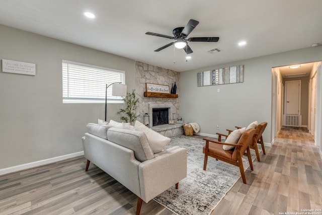 living area featuring visible vents, a stone fireplace, light wood-style flooring, and baseboards