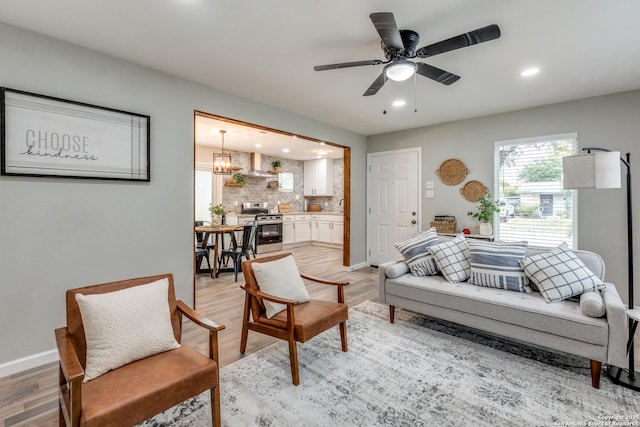 living room featuring ceiling fan with notable chandelier, recessed lighting, light wood-type flooring, and baseboards