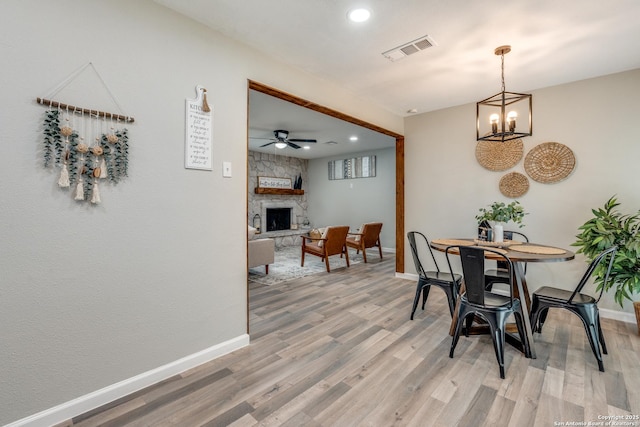 dining space with light wood-style floors, baseboards, visible vents, and a stone fireplace