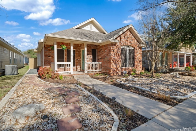 view of front facade featuring cooling unit, brick siding, a porch, and roof with shingles