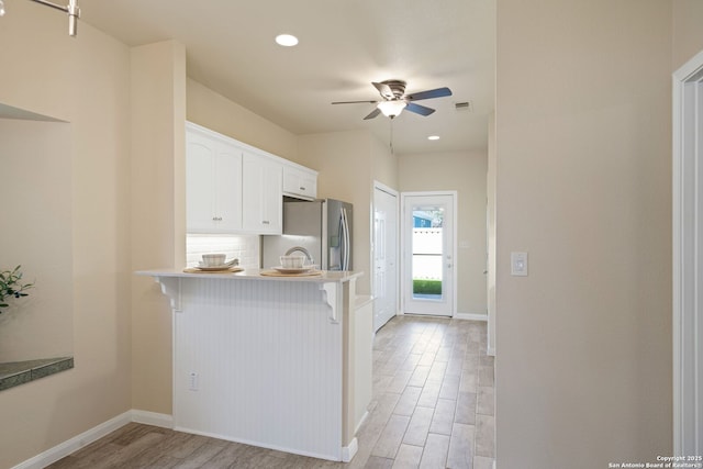 kitchen with a kitchen bar, light wood-style flooring, stainless steel refrigerator with ice dispenser, white cabinets, and decorative backsplash