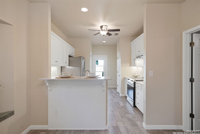 kitchen with tasteful backsplash, under cabinet range hood, electric stove, freestanding refrigerator, and white cabinets