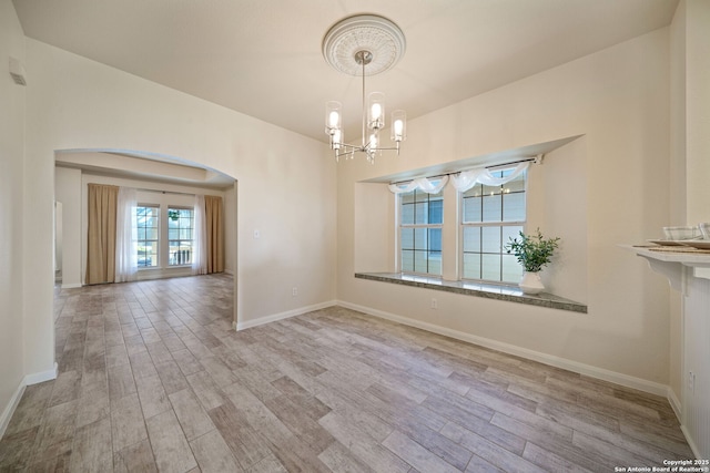 unfurnished dining area featuring baseboards, arched walkways, an inviting chandelier, and wood finished floors