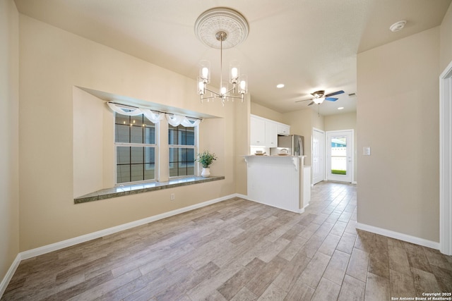 interior space featuring baseboards, light wood finished floors, white cabinets, stainless steel refrigerator with ice dispenser, and decorative light fixtures