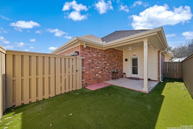 rear view of property featuring a lawn, a ceiling fan, a fenced backyard, brick siding, and a patio area