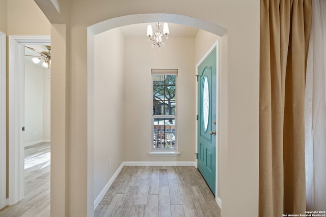 foyer featuring baseboards, arched walkways, and light wood-style floors