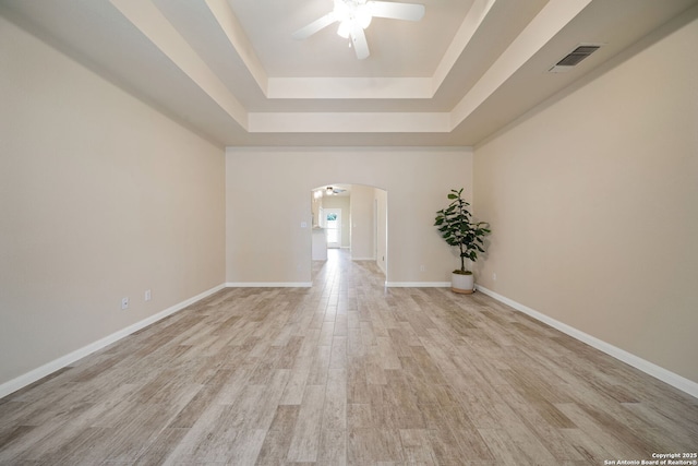 empty room with visible vents, light wood-style flooring, arched walkways, baseboards, and ceiling fan