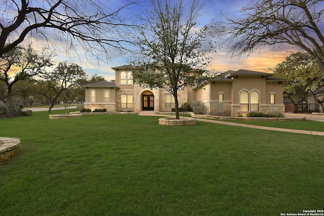 mediterranean / spanish-style house with a yard, stone siding, and stucco siding