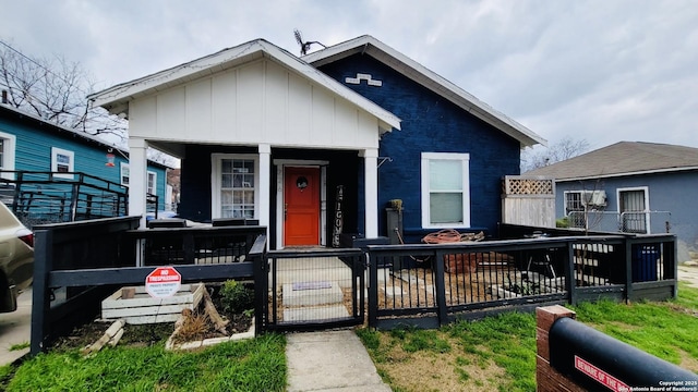 bungalow-style house with a fenced front yard, covered porch, board and batten siding, and a gate