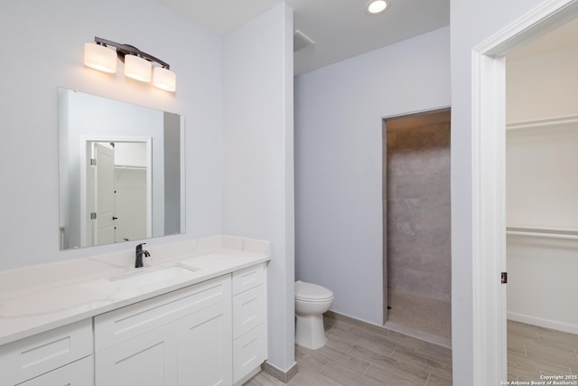 full bath featuring baseboards, toilet, wood tiled floor, a walk in closet, and vanity