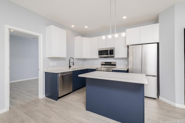 kitchen with light wood finished floors, stainless steel appliances, white cabinetry, a sink, and a kitchen island