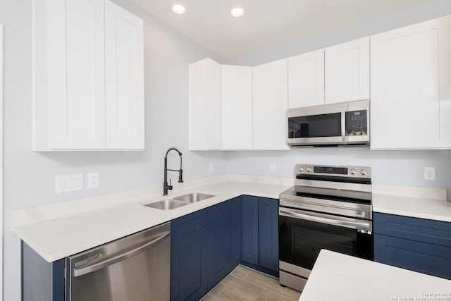 kitchen with appliances with stainless steel finishes, blue cabinets, a sink, and white cabinetry