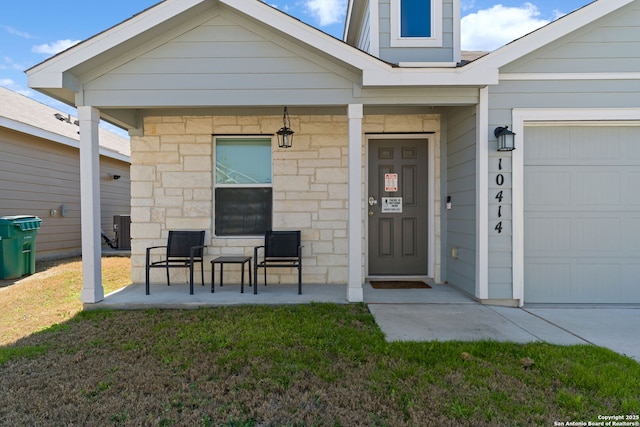 view of exterior entry featuring an attached garage, stone siding, and a yard