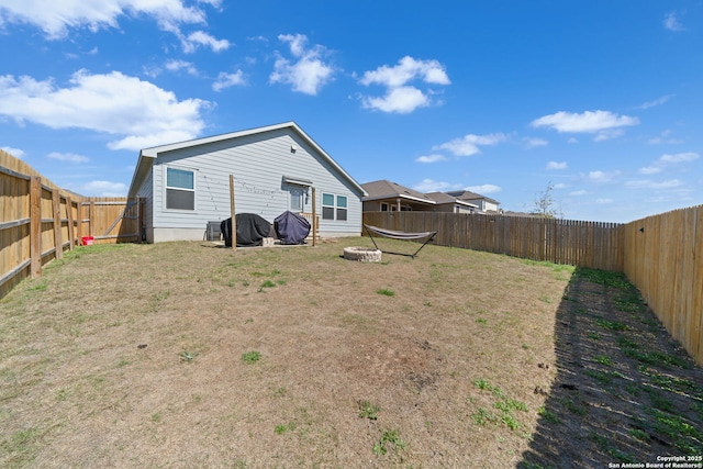 rear view of house with a yard, an outdoor fire pit, and a fenced backyard