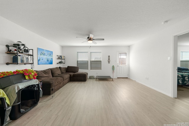 living room featuring light wood-style flooring, baseboards, ceiling fan, and a textured ceiling