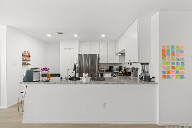 kitchen with under cabinet range hood, stainless steel appliances, a sink, visible vents, and light stone countertops