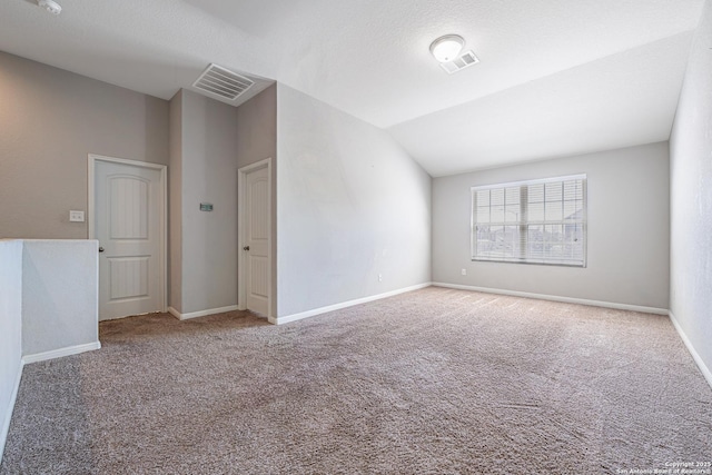carpeted empty room with visible vents, vaulted ceiling, and baseboards