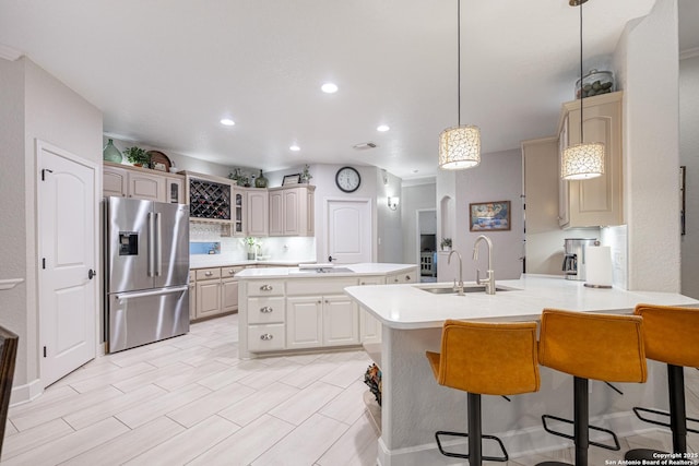 kitchen with a peninsula, a sink, a kitchen island, light countertops, and stainless steel fridge