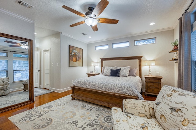 bedroom featuring baseboards, visible vents, ornamental molding, wood finished floors, and a textured ceiling