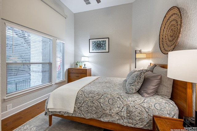 bedroom featuring a textured wall, wood finished floors, and baseboards