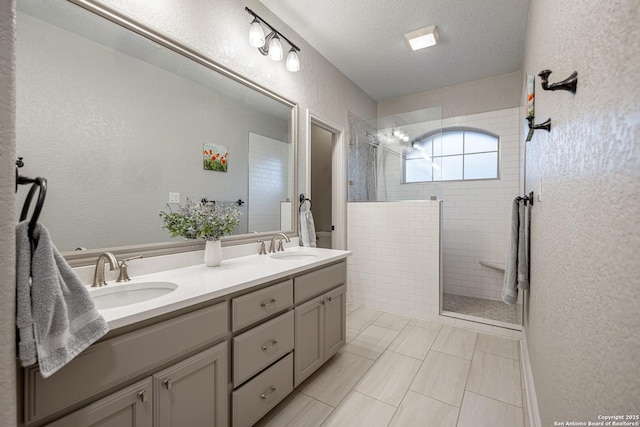 full bath featuring a textured ceiling, a walk in shower, a textured wall, a sink, and double vanity