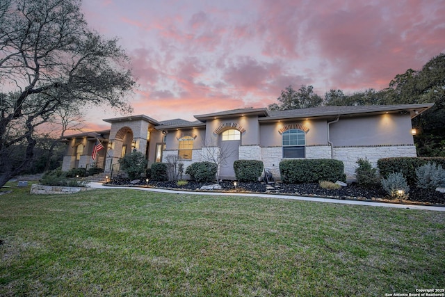 view of front of property featuring stone siding, a front yard, and stucco siding