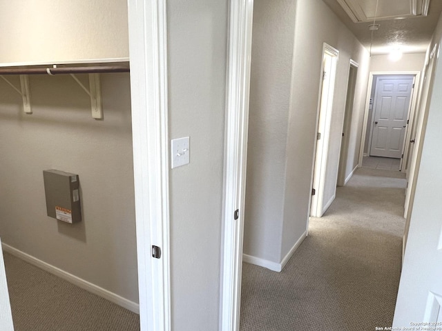 hall featuring attic access, carpet flooring, and baseboards