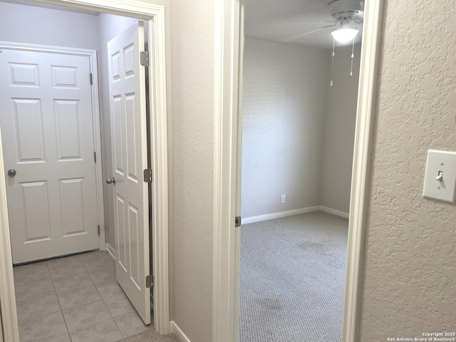 hall with light colored carpet, a textured wall, and light tile patterned floors