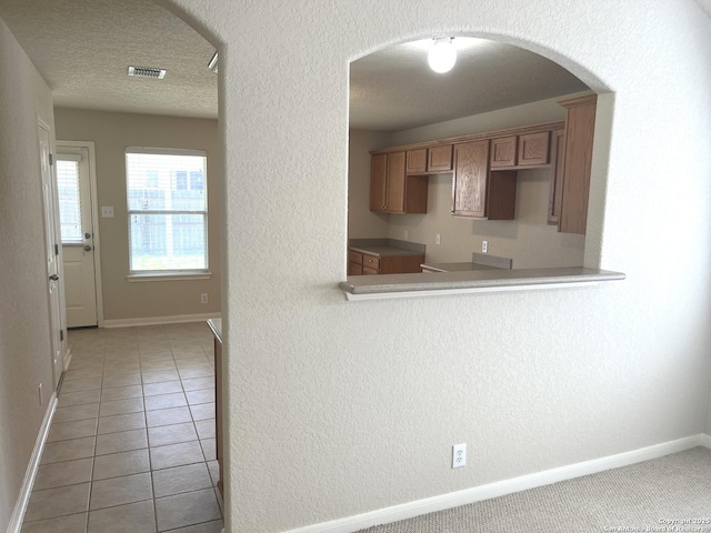 kitchen with arched walkways, a textured ceiling, light tile patterned flooring, visible vents, and baseboards