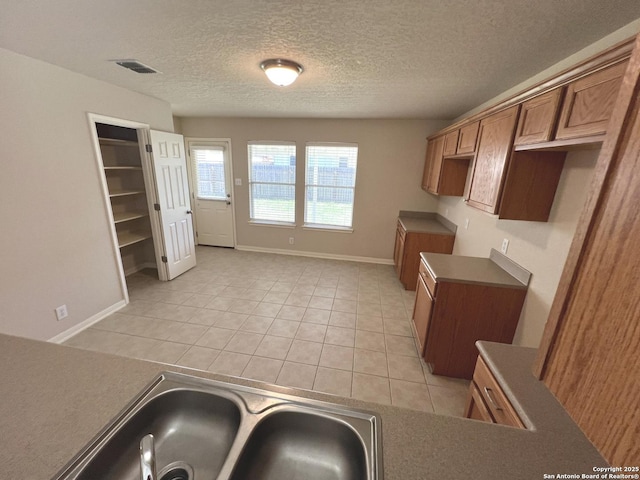 kitchen with light tile patterned floors, visible vents, brown cabinets, a textured ceiling, and a sink