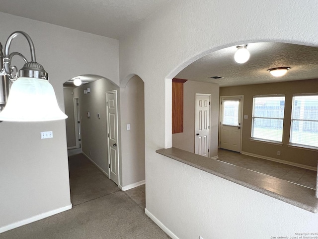 hall featuring baseboards, visible vents, arched walkways, a textured ceiling, and carpet flooring