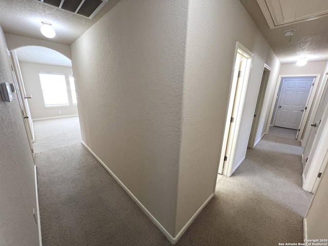 hall featuring attic access, a textured ceiling, arched walkways, and carpet flooring